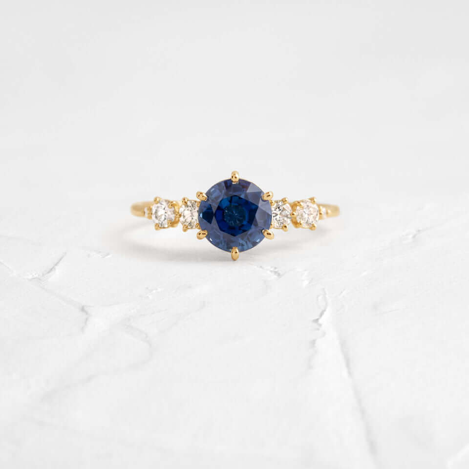 This engagement ring features 925 sterling silver with yellow gold plating, set with a deep blue round cut blue stone, exuding classic and noble elegance