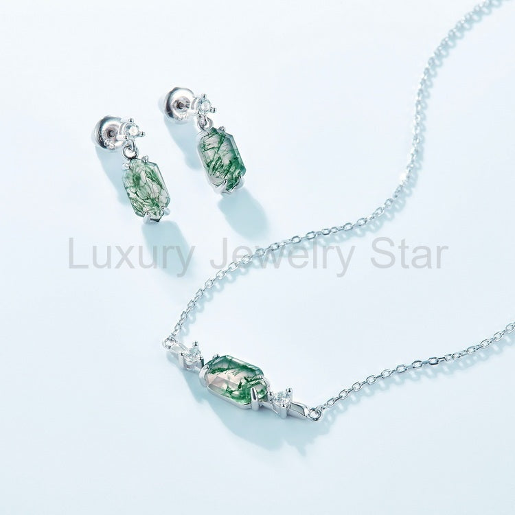 Green centerpiece necklace displayed beside a pair of drop earrings on a pale blue surface.