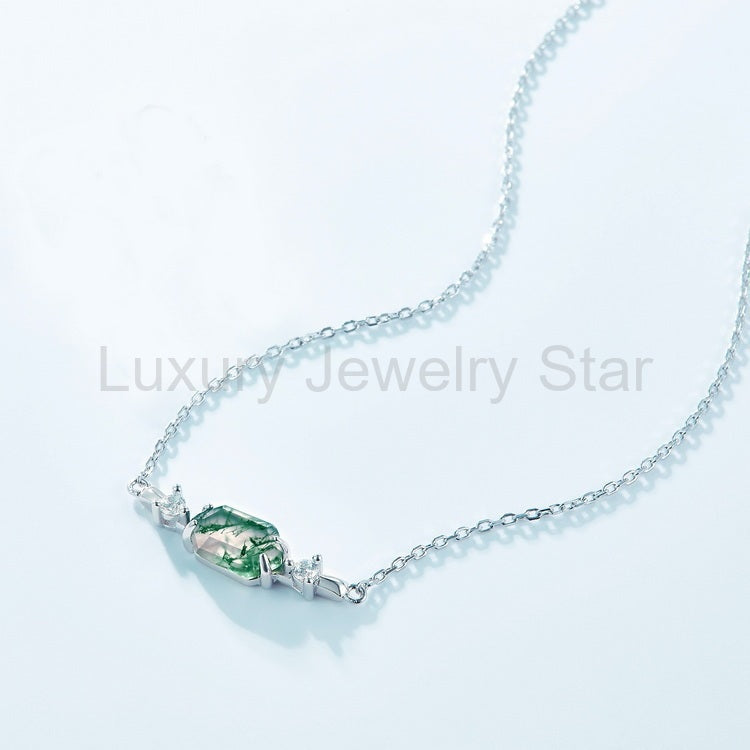 Angled view of a green centerpiece necklace with a silver-tone chain on a pale blue surface.