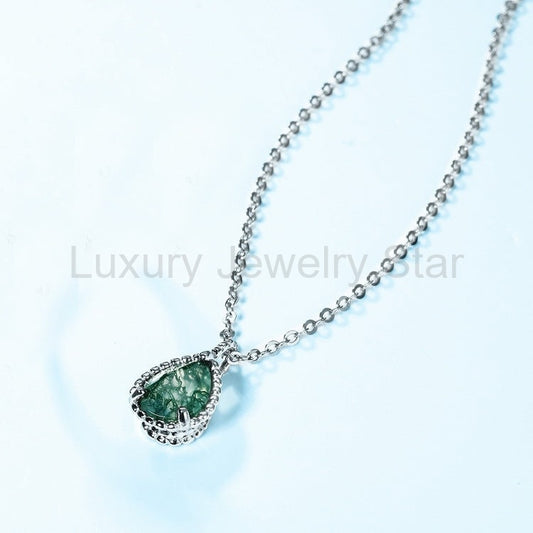 Pear-shaped green pendant with a silver-tone beaded edge and chain arranged diagonally on a pale