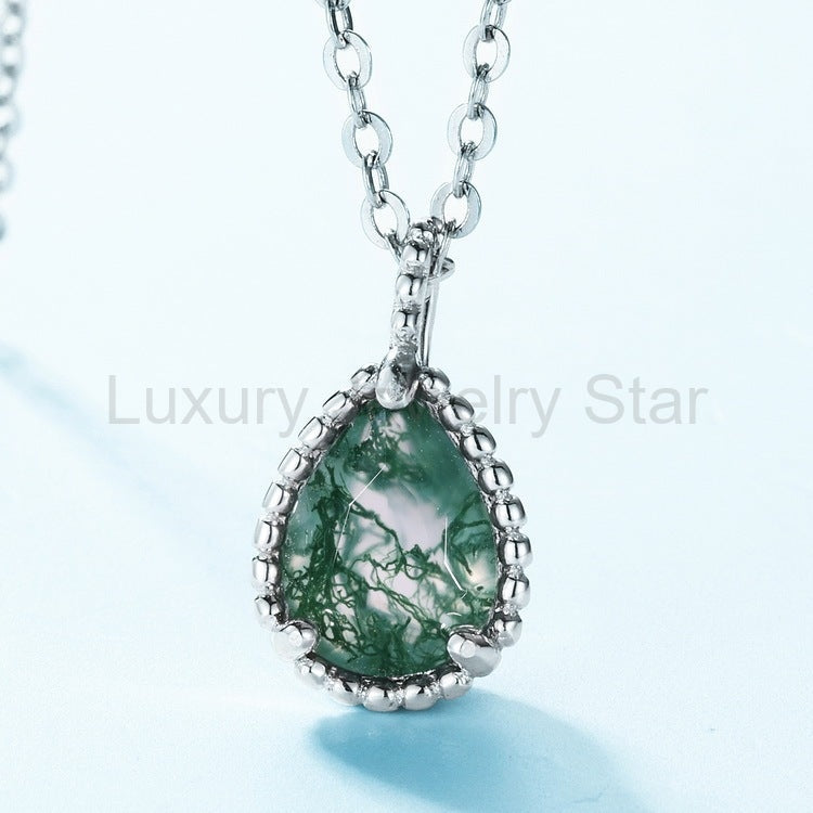 Close-up of branching green patterns, silver-tone prongs and a beaded border on a pear-shaped