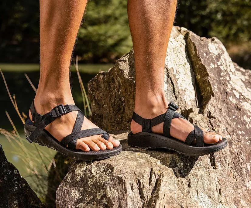 Man wearing Chaco Z2 Classic sandals while standing on rocks near water, ideal for water sports and
